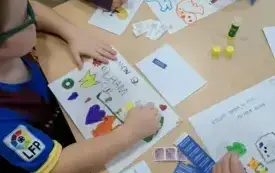 dzieci siedzą przy stoliku przed nimi rysunki i przypory plastyczne