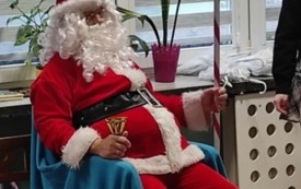 święty mikołaj siedzi na niebieskim fotelu przed nim dzieci ubrane w czapki mikołajowe
