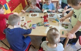 dzieci siedzą przy stoliku i dekorują pierniki za pomocą lukrowych pisak&oacute;w