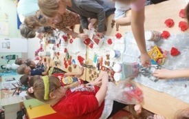 dzieci siedzą wzdłuż stoł&oacute;w na kt&oacute;rych leżą foremki, ściereczki i przybory do zabawy z piernikami dzieci wykrawają pierniki obok pani kt&oacute;ra pomaga jednemu z dzieci