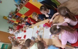 dzieci siedzą wzdłuż stoł&oacute;w na kt&oacute;rych leżą foremki, ściereczki i przybory do zabawy z piernikami