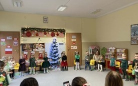 dzieci stoją w p&oacute;łkolu przy ż&oacute;łtych krzesełkach widać panie w tle dekoracja świąteczna