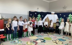 dzieci w odświętnych strojach stoją w p&oacute;łkolu za nimi świąteczno zimowa dekoracja
