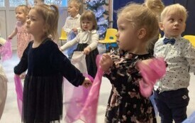 dzieci w odświętnych strojach stoją na dywanie trzymają kolorowe chusteczki w tle dekoracja z sercami