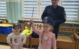dwie dziewczynki w czapkach policyjnych za dziewczynkami stoi pan policjant