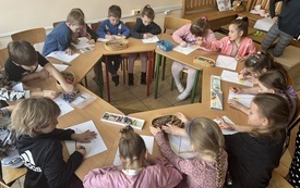 dzieci siedzą przy stolikach ustawionych w koło każde dziecko koloruje obrazek w kształcie dużego kolca
