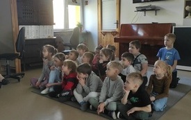 dzieci siedzą na dywanie w grupie obok nich pani