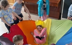dzieci trzymają chustę animacyjną na chuście siedzi tr&oacute;jka dzieci