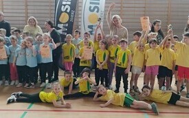 dzieci w strojach sportowych pozują do zdjęcia wśr&oacute;d nich panie w tle sala sportowa