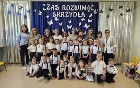 grupa dzieci w odświętnych strojach pozuje wraz z nauczycielkami do zdjęcia grupowego w tle dekoracja na zakończenie roku