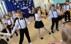 grupa dzieci w odświętnych strojach w tańcu w tle dekoracja na zakończenie roku szkolnego