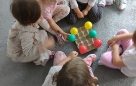 dzieci siedzą wok&oacute;ł wytłaczanki po jajkach na kt&oacute;rej leżą kolorowe piłeczki