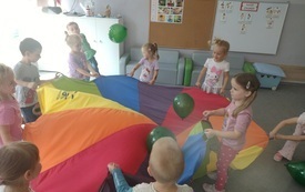 dzieci trzymają dookoła chustę animacyjną na kt&oacute;rej znajdują się balony