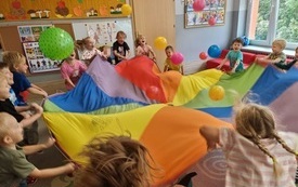 dzieci podrzucają piłki i balony na kolorowej chuście animacyjnej