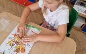 dziewczynka siedzi przy stoliku przed nią leży praca plastyczna w jesiennych kolorach w kształcie drzewa