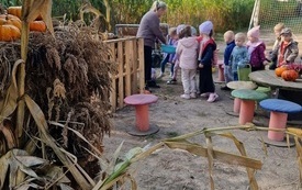 dzieci stoją w rzędzie przed nimi pani dookołą sceneria jesienna