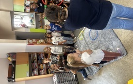 dzieci stoją w kole wśr&oacute;d nich stoją dwie panie na dywanie na środku leżą kolorowe obręcze