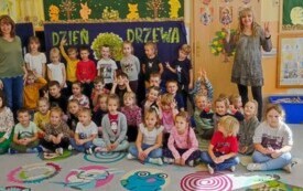 dzieci siedzą na dywanie nauczycielki stoją po prawej i lewej stronie w tle napis dzień drzewa
