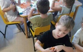 dzieci siedzą przy stolikach i wycinają kolorowe liście