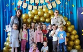 grupa dzieci pozuje do zdjęcia po bokach panie nauczycielki w tle złote balony i dekoracja Dzień Edukacji Narodowej
