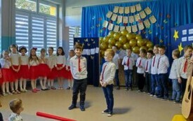 dw&oacute;ch chłopc&oacute;w w odświętnych strojach stoją na środku sali w tle pozostałe dzieci po bokach panie nauczycielki 