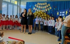dwie panie nauczycielki na środku sali z mikrofonem w tle odświętnie ubrana grupa dzieci