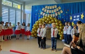 trzech chłopc&oacute;w z mikrofonami na środku sali w tle pozostałe dzieci po bokach panie nauczycielki z gitarami 