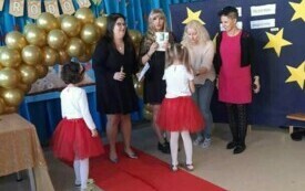na czerwonym dywanie trzy nauczycielki z grupy V w towarzystwie pani dyrektor dwie dziewczynki stoją zwr&oacute;cone w stronę pań w tle złote balony i napis Dzień Edukacji Narodowej