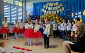dwie dziewczynki i chłopiec w odświętnych strojach stoją na środku sali w tle pozostałe dzieci po bokach nauczycielki z gitarami