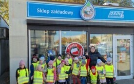 grupka dzieci wraz z nauczycielką na tle sklepu mleczarskiego