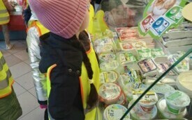 grupka dzieci przygląda się produktom mleczarskim znajdującym sie za szklaną ladą w sklepie