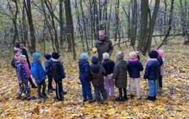  nauczycielka i grupa dzieci stoi przed panem przewodnikiem dookoła dużo ż&oacute;łtych liści pan przewodnik trzyma liść klony