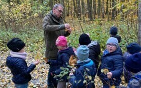 grupa dzieci  z panem przewodnikiem w tle las z ż&oacute;łtymi liśćmi