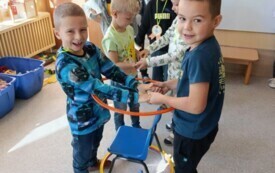 dw&oacute;ch chłopc&oacute;w trzyma obręcz nad krzesełkami w tle dzieci