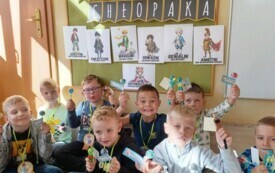 grupka chłopc&oacute;w siedzi na dywanie w dłoniach trzymają lizaki z etykietką w tle napis dzień chłopaka i postacie na obrazkach