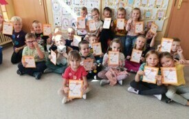 grupa dzieci siedzi na dywanie dzieci trzymają dyplomy w tle dekoracja na dzień kropki