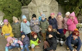 Dzieci klekają i stoja przed pomnikiem na cmentarzu