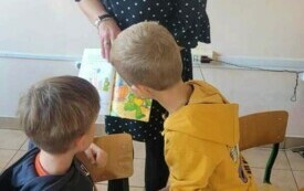 Chłopcy przyglądają sie obrazkom w książce trzymanej przez panią.