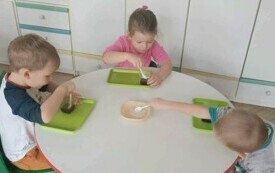 Dzieci siedzą przy stole, wykonując zadanie. 