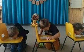 Trzech chłopc&oacute;w zlizuje mi&oacute;d z talerzyk&oacute;w stojących na krzesłach. 