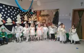 dziewczynki w przebraniach aniołk&oacute;w trzymają w dłoniach złote dekoracje w tle świąteczne motywy