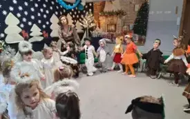 dzieci w przebraniach trzymają się za ręce wraz z nauczycielką w kole w tle świąteczna dekoracja