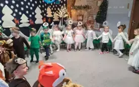 dzieci w przebraniach trzymają się za ręce w kole w tle świąteczna dekoracja