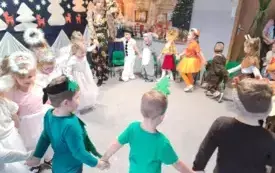 dzieci w przebraniach trzymają się za ręce w kole w tle świąteczna dekoracja