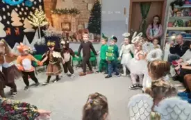 dzieci w przebraniach trzymają się za ręce w kole w tle świąteczna dekoracja