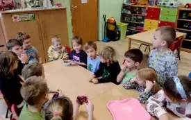 grupa dzieci siedzi przy złaczonych stołach