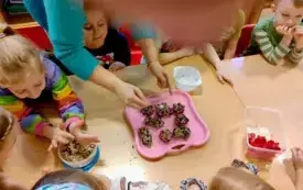 dzieci siedza przy stole na stole wiadereczko z ziarnami nauczyciel wkłada ziarna do foremek