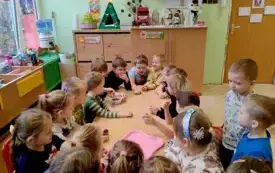 grupa dzieci siedzi przy złączonych stołach chłopiec trzyma miseczkę z mieszanką ziaren