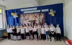 grupa dzieci w odświętnych strojach z czapkami absolwentów na głowach pozuje do zdjęcia w tle dekoracja zakończenie przedszkola 2025