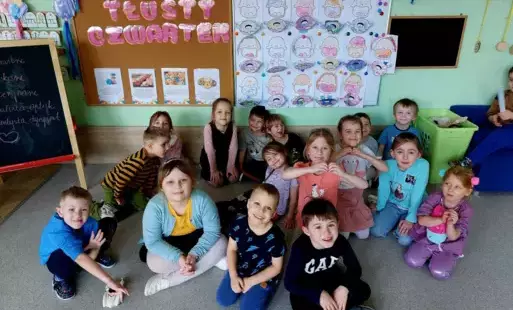 grupa dzieci siedzi na dywanie pozuje do zdjęcia w tle dekoracja tłusty czwartek